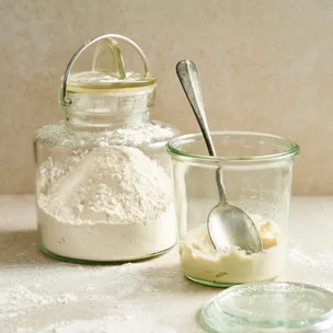 A jar of sourdough starter with a spoon and container of flour