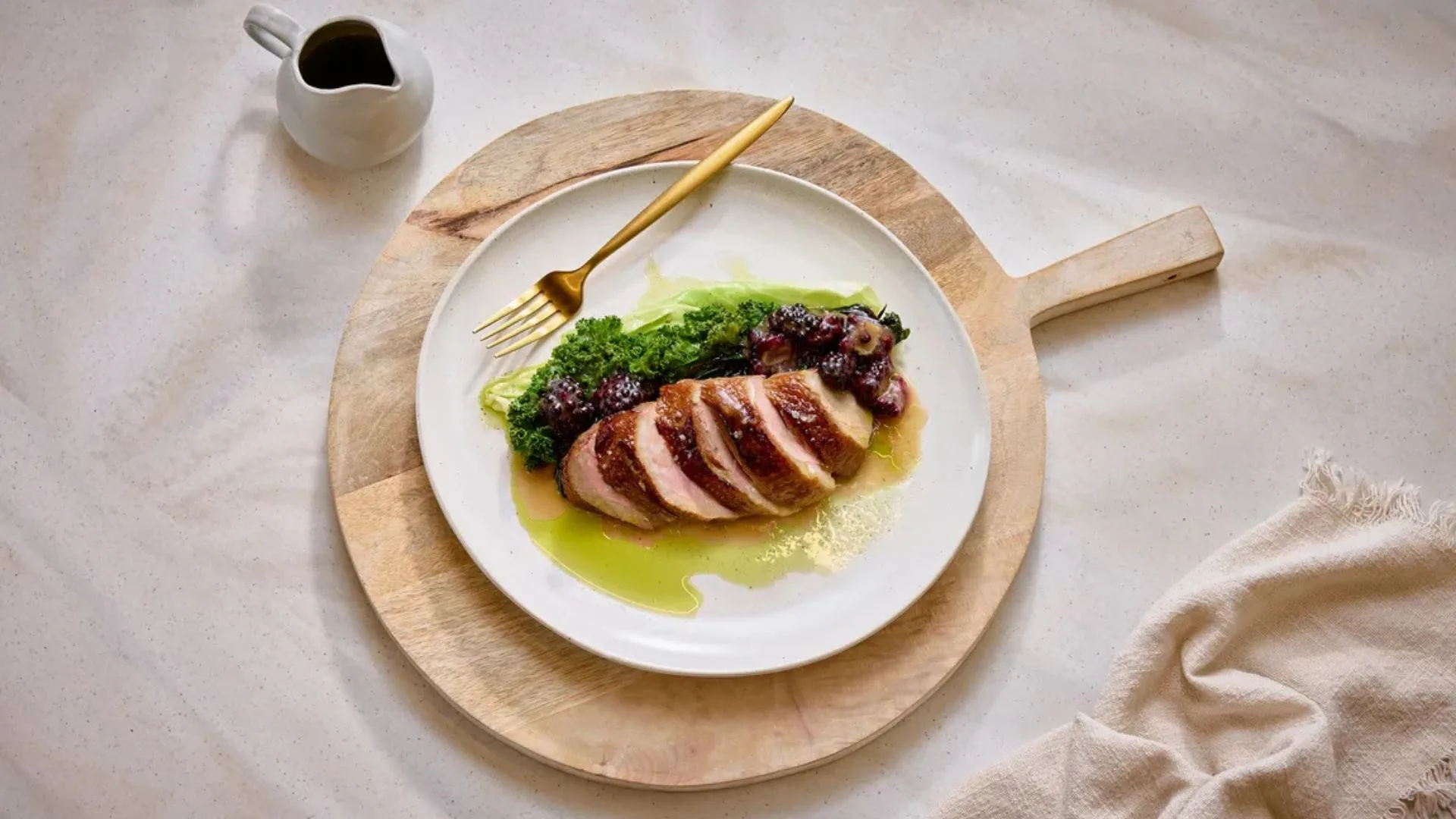 Sliced crispy duck breast with steamed greens and blackberry sauce on a white plate.