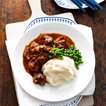 Julie Goodwin's Braised steak and onions on a white plate with mashed potato and peas