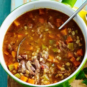 Lamb shank and barley soup in a large pot with a metal spoon