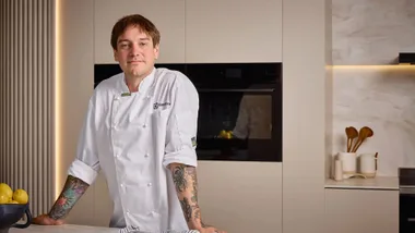 Australian chef Matt Stone in a white chef jacket standing in a modern kitchen with a black integrated Electrolux oven, ready to share his favorite steam oven recipes.