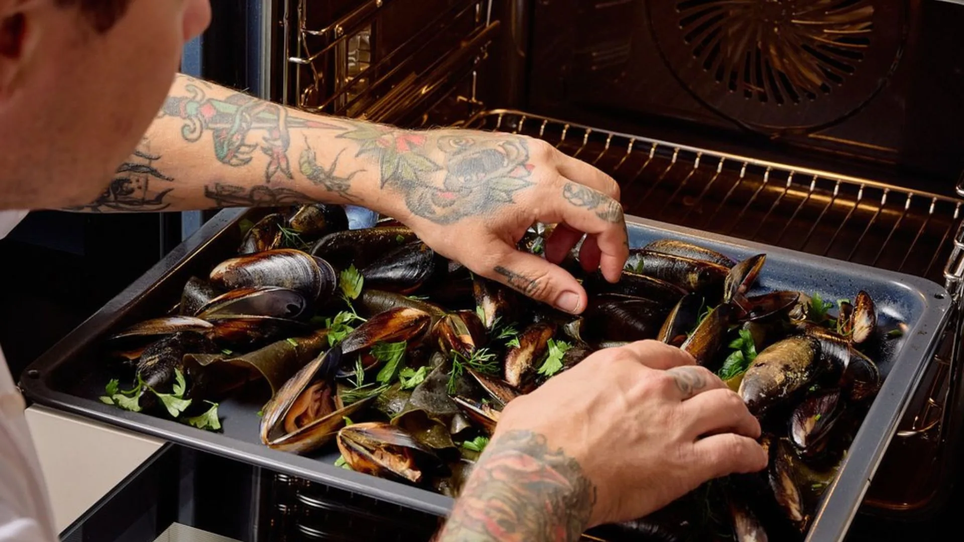 Chef Matt Stone sliding a tray of fresh seafood and herbs into the appliance, showing how to cook effortless steam oven recipes like his steamed mussels with brown butter.