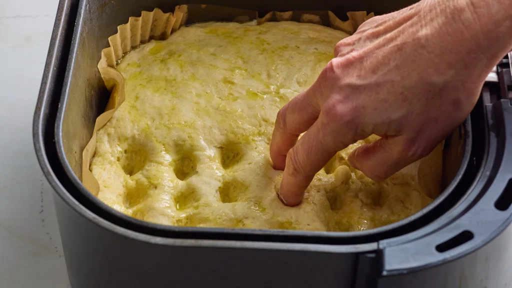 a hand pressing dimple into focaccia dough
