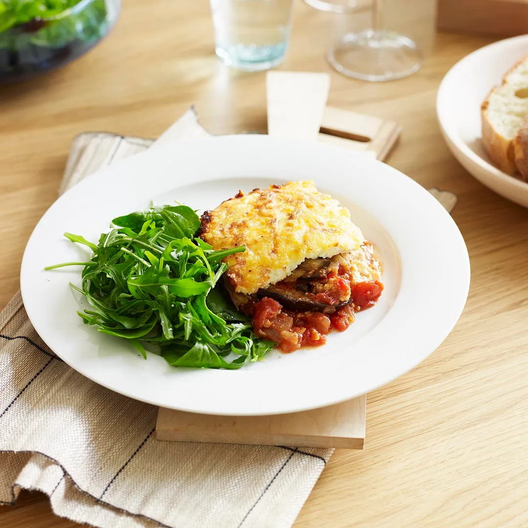 A slice of cheesy baked eggplant on a plate with greens