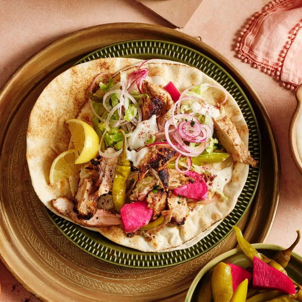 chicken shawarma wrap with bowls of vegetables and dip