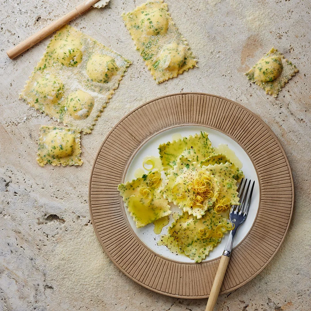 Parmigiano Regginao ravioli in a bowl with uncooked ravioli on the bench