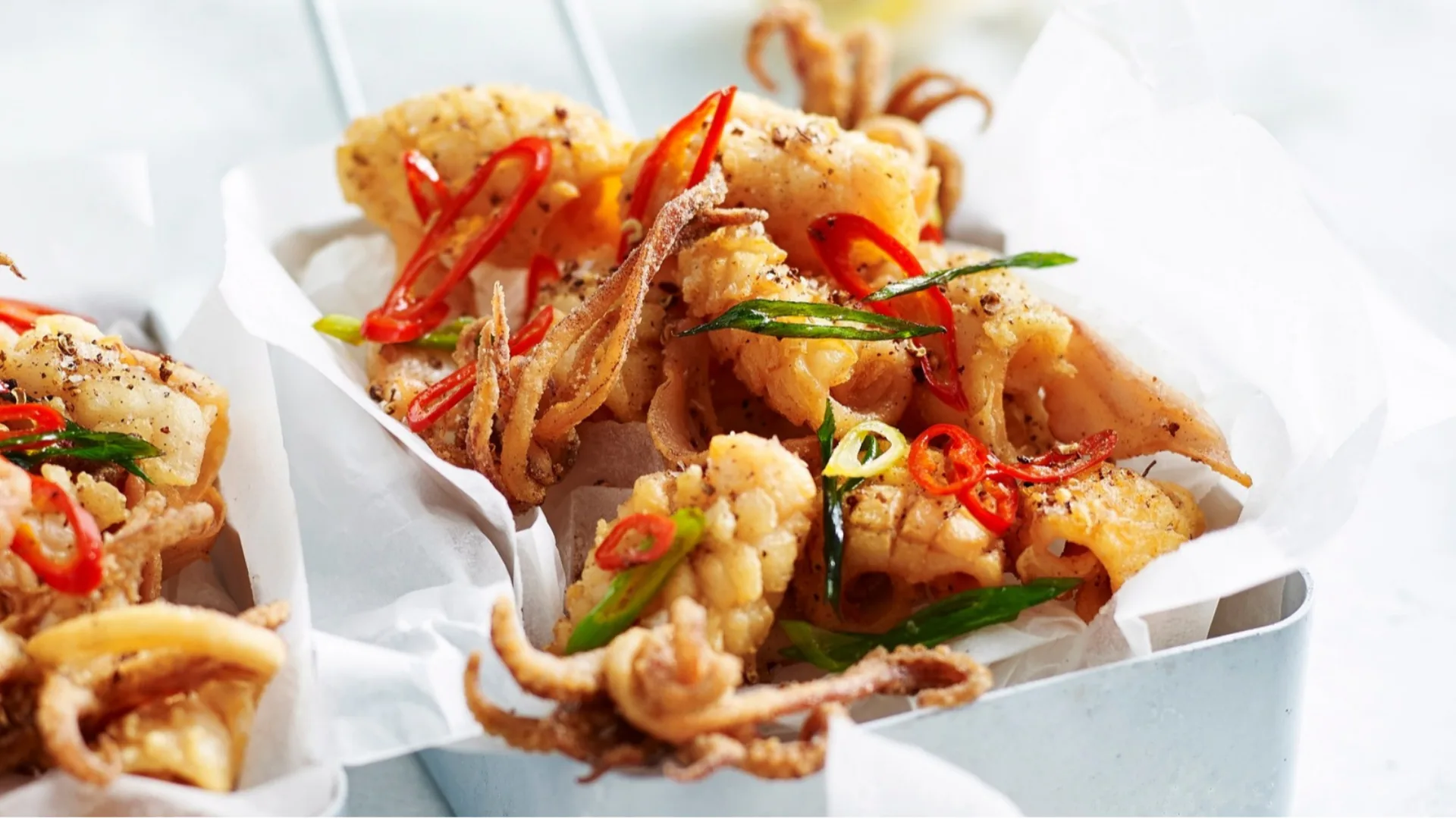 salt and pepper squid in a container topped with red chilli and green onion