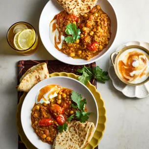 two bowls of vegetarian chickpea and lentil curry with naan and mango chutney