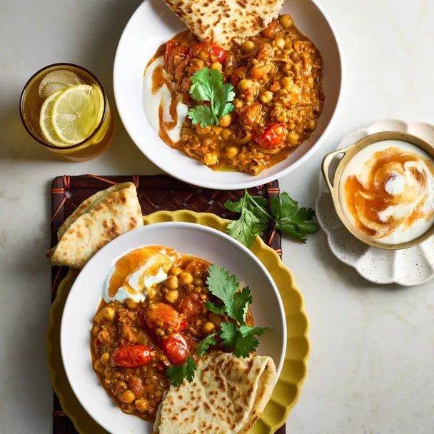 two bowls of vegetarian chickpea and lentil curry with naan and mango chutney