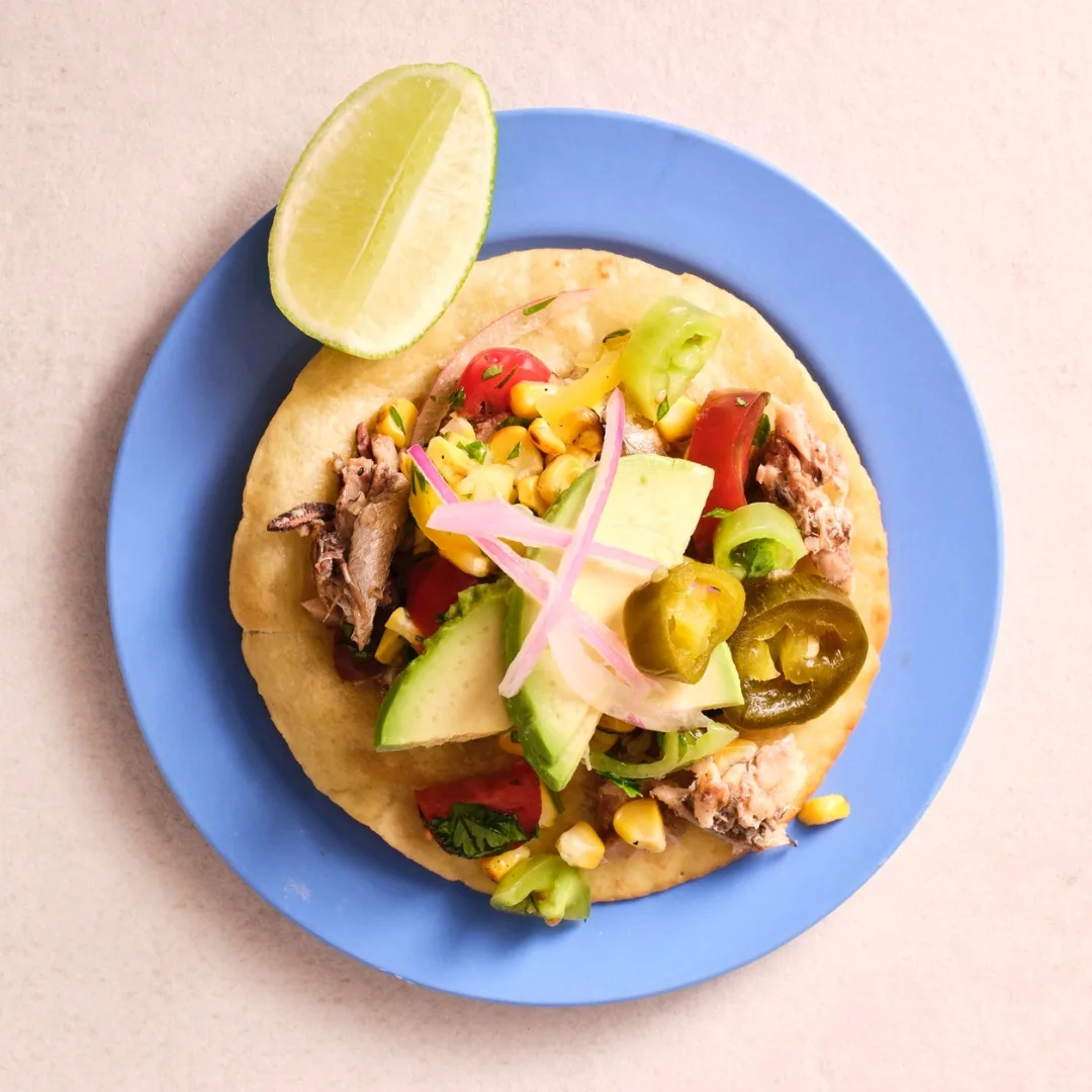 mexican sardine tostada on a blue plate with a lime wedge