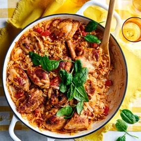 Spiced chicken pilaf with browned chicken, rice, onions, tomatoes, and fresh spinach in a white serving dish.
