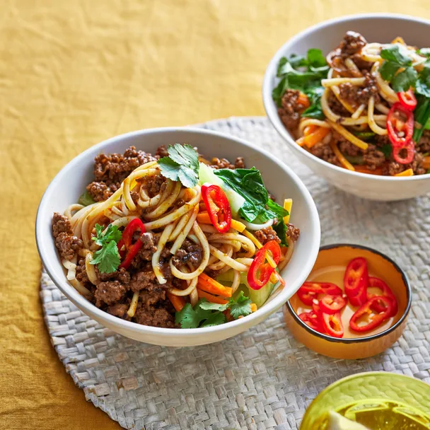 Spicy beef noodles with bok choy, coriander, and red chili, served in a bowl with lime and extra chili on the side.