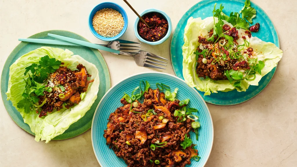 three plates with san choy bow beef lettuce cups, and two small bowls with sesame seeds and chilli paste