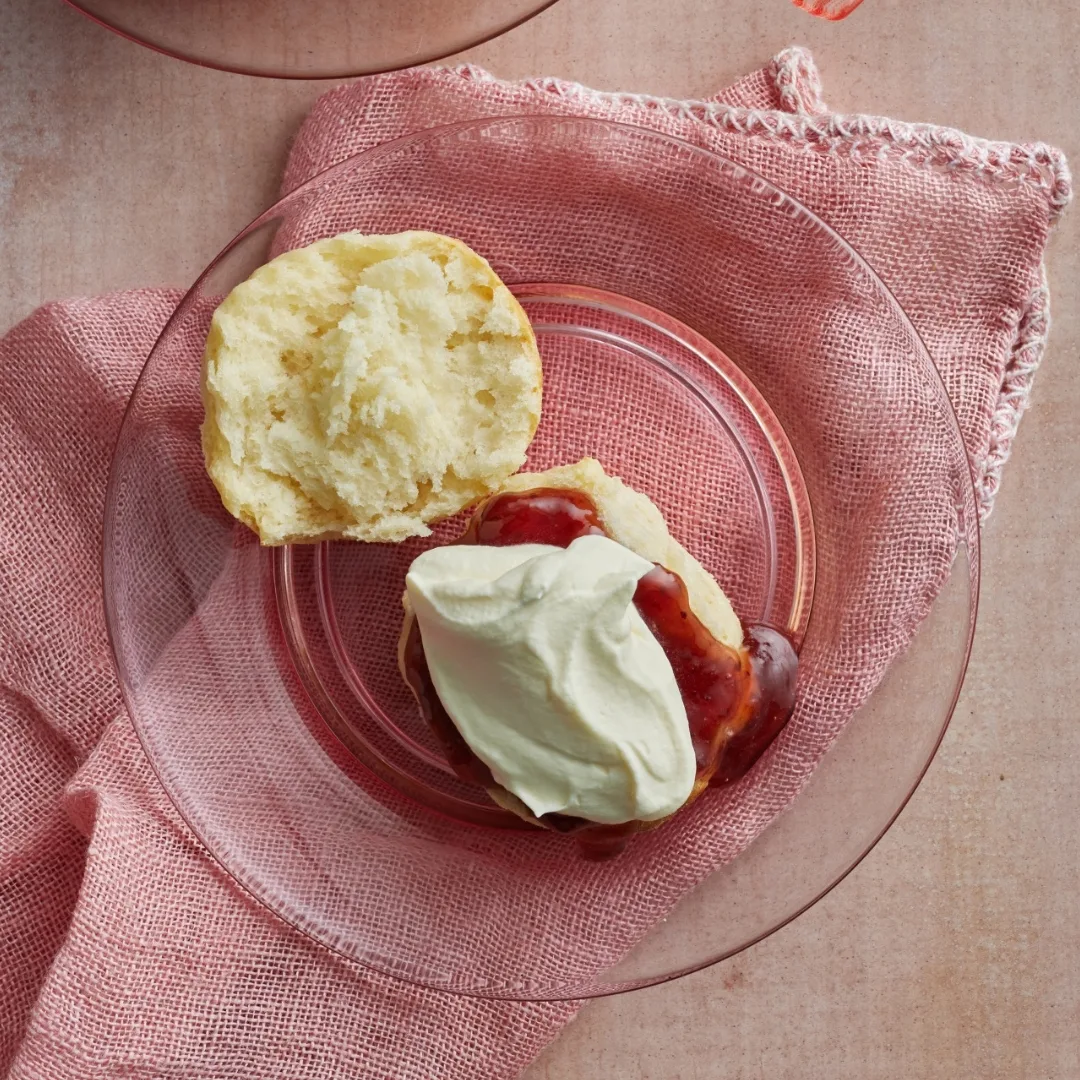 a scone on a glass plate with jam and cream