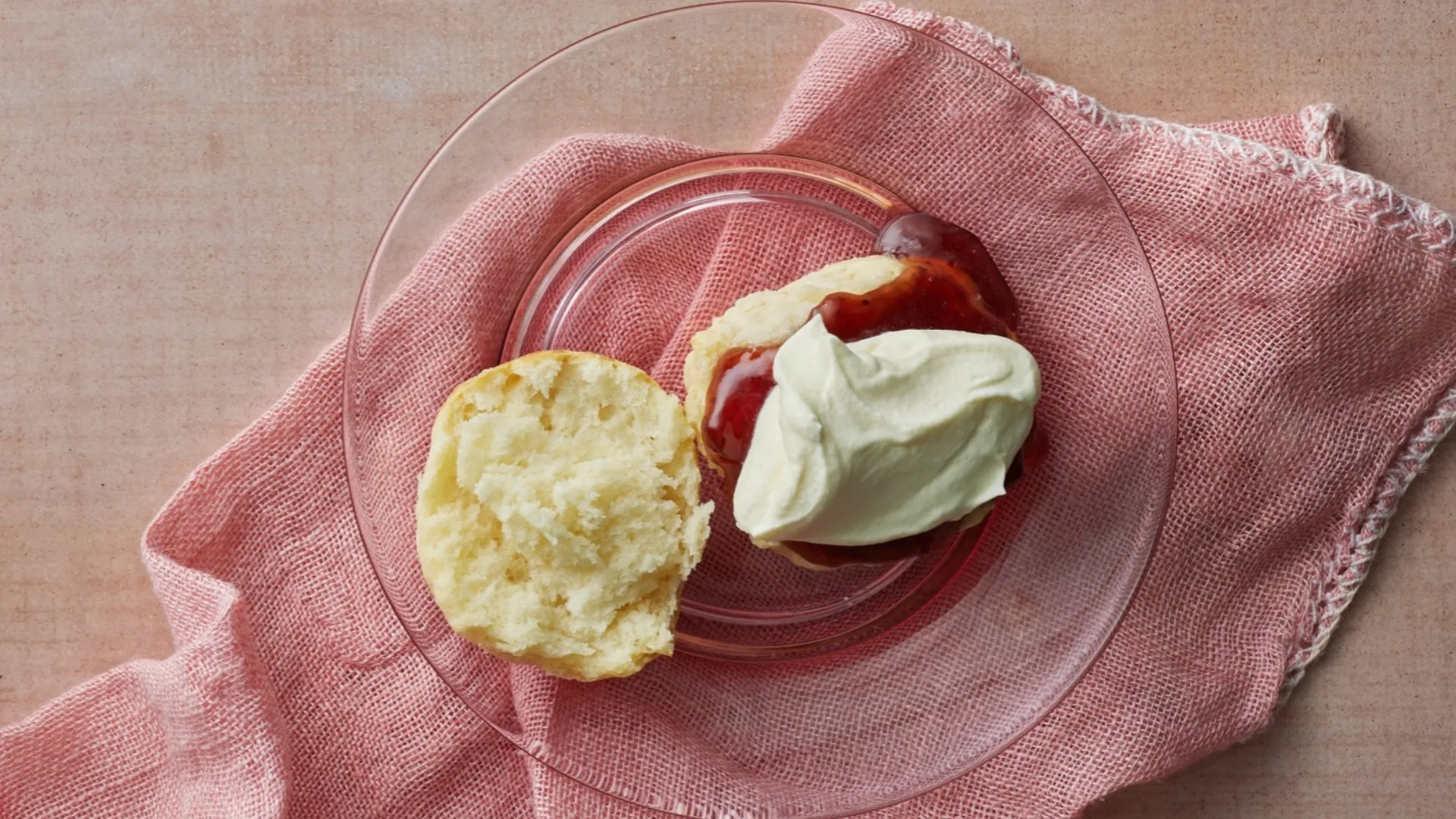 scone cut in half on a plate with jam and cream