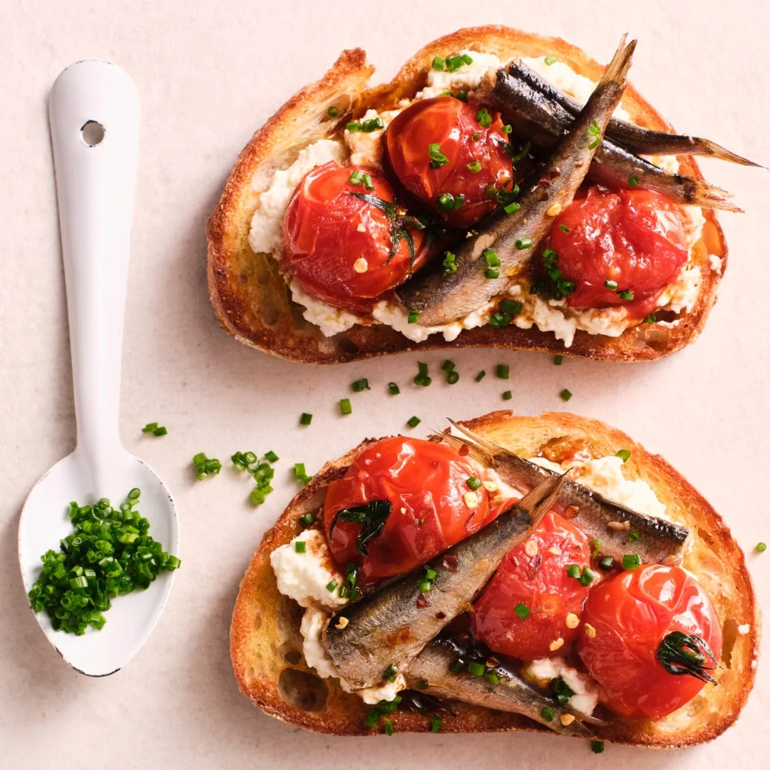 Smoked sardine & blistered tomato toasts with a spoon filled with chopped herbs