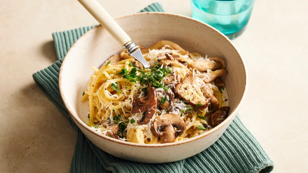 spaghetti cacio e pepe with mushrooms and herbs in a bowl with a fork