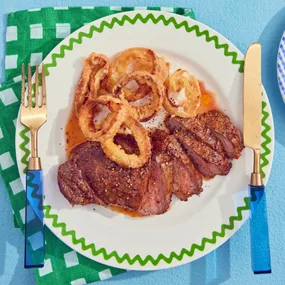 air fryer steak with onion rings on a plate with a knife and fork