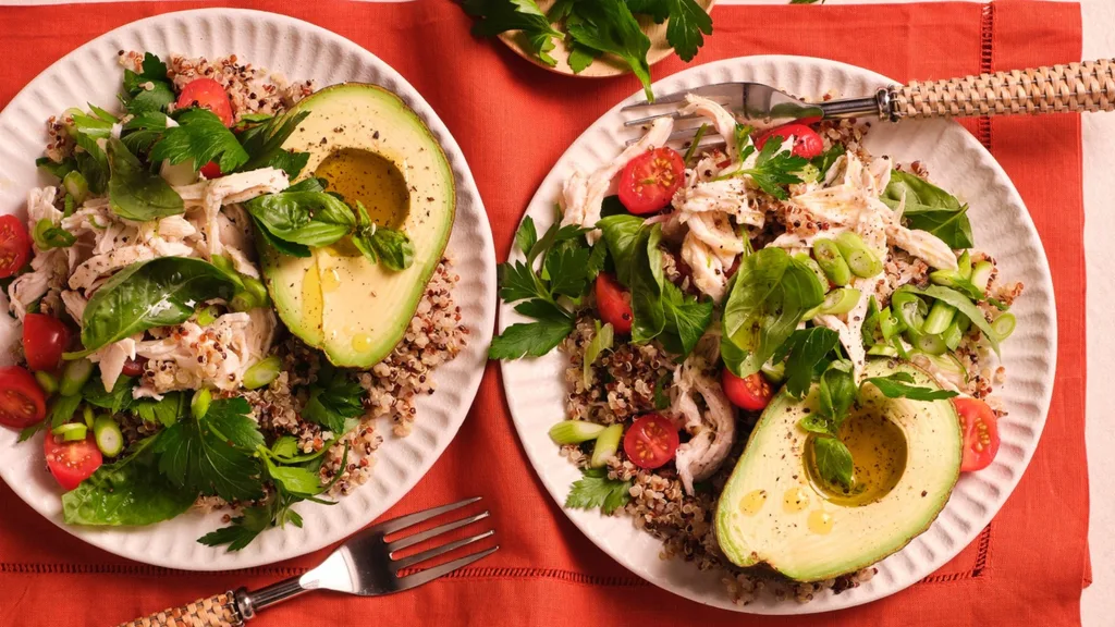 two plates of poached chicken quinoa salad with avocado, tomato and herbs