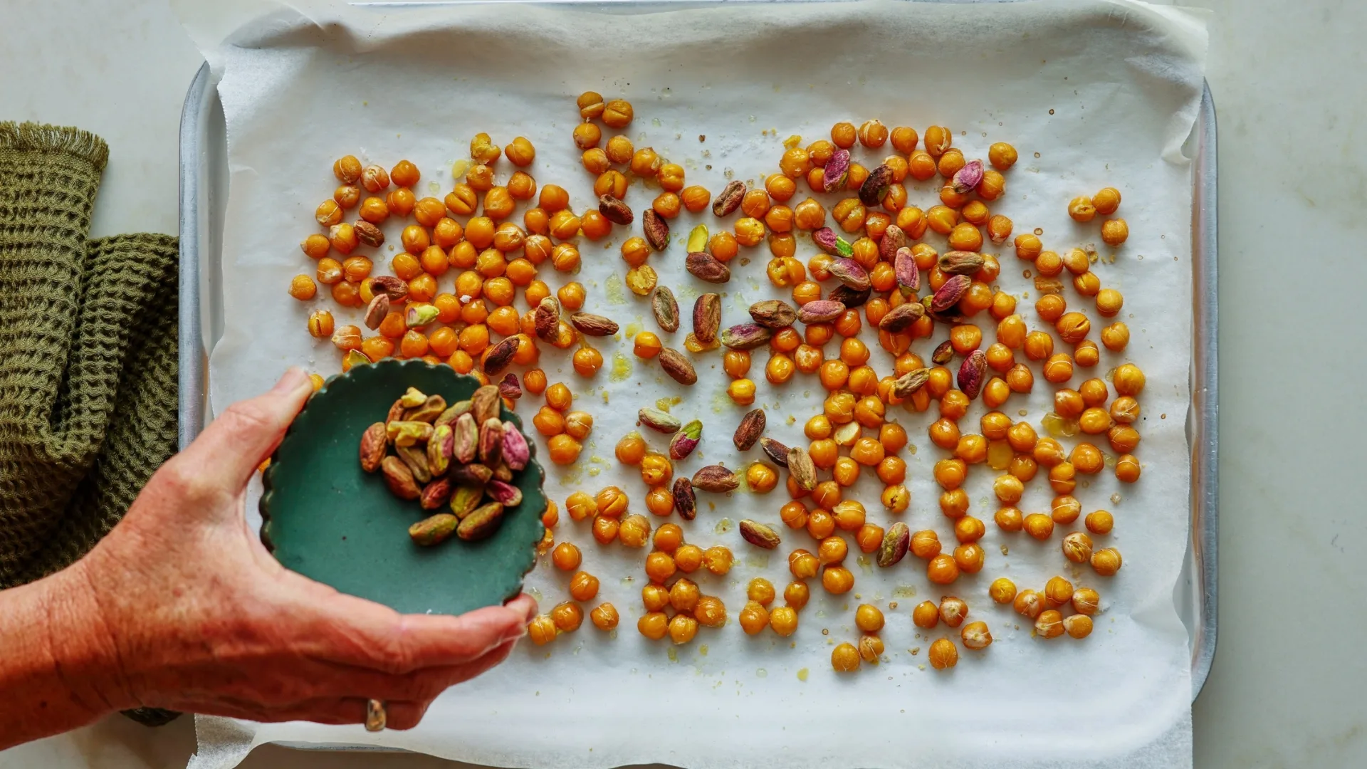 roasted chickpeas on a tray and a hand holding a bowl of pistahchios
