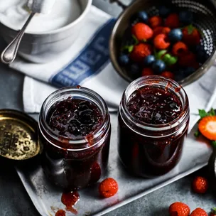 two jars of slow cooker mixed berry jam with a bowl of sugar and strainer of berries