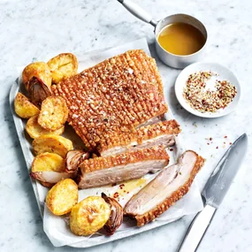 air fryer pork roast on a tray with roast potatoes and onion, with a pot of gravy