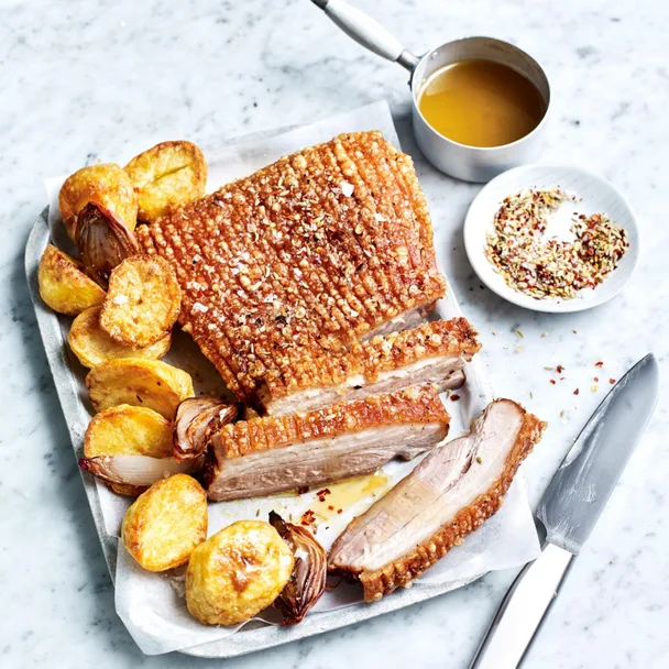 air fryer pork roast on a tray with roast potatoes and onion, with a pot of gravy