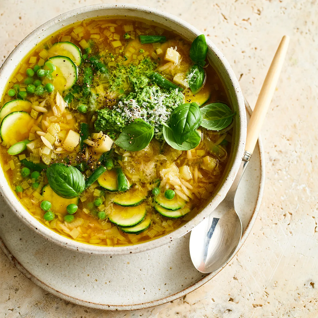 Bowl of spring vegetable minestrone soup garnished with pesto