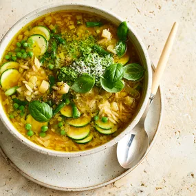 Bowl of spring vegetable minestrone soup garnished with pesto