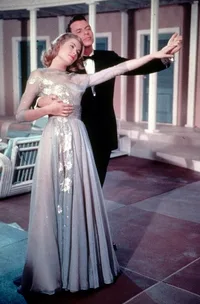 Grace Kelly in a stunning silver gown, dancing with a man in a tuxedo, in a scene from a classic film.