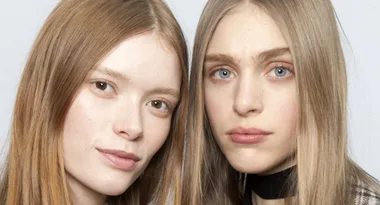 Two young women with long hair, looking directly at the camera. The woman on the left has auburn hair, and the woman on the right has blonde hair.