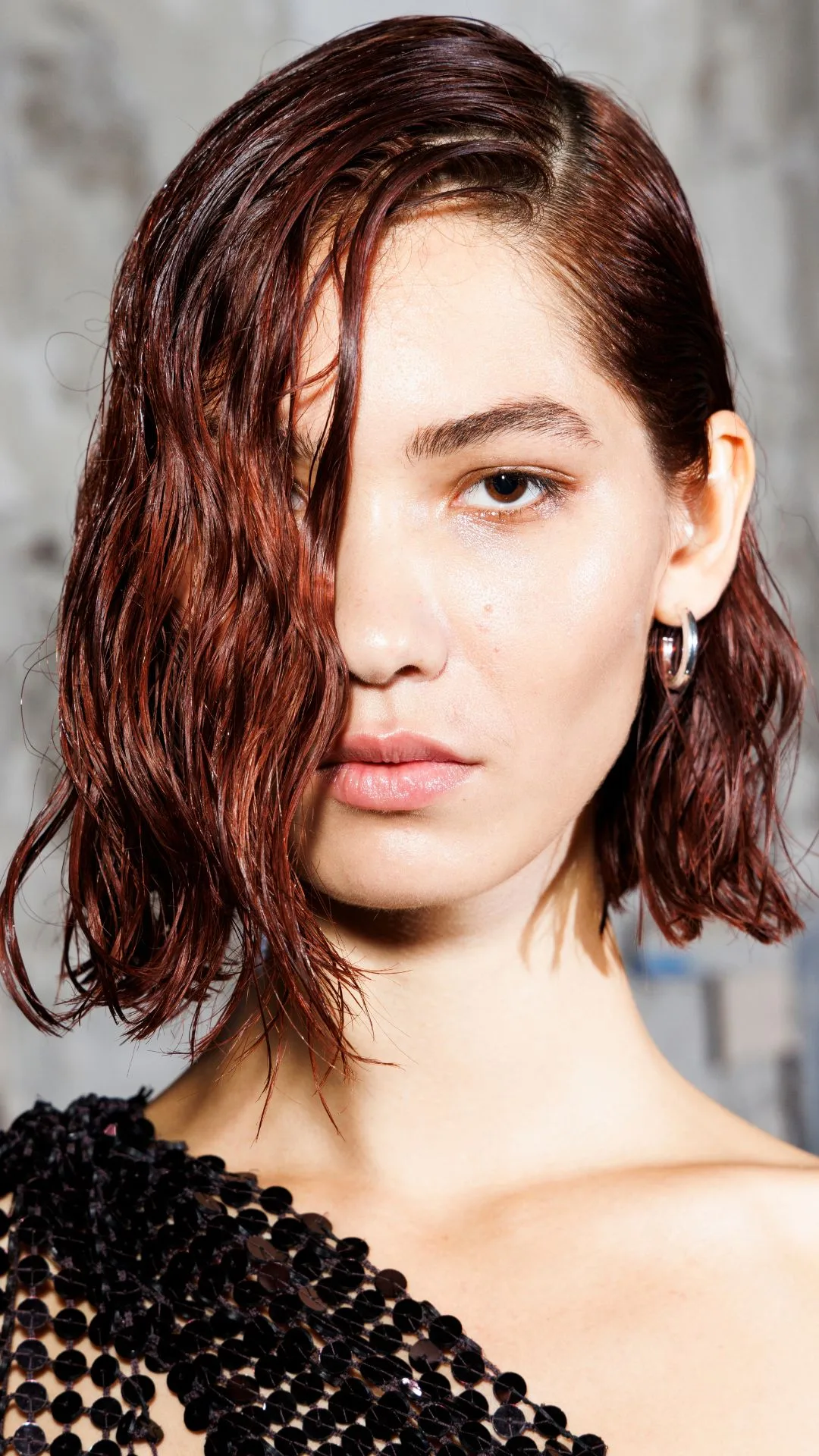 Rayssa Medeiros is seen backstage at the The Attico fashion show during the Milan Womenswear Spring/Summer 2025. The model is shot in a close up angle showing mostly her face with a wet look auburn bob hair cut covering half of her face. 