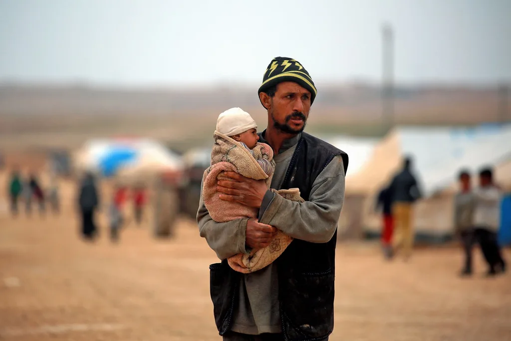 A displaced Syrian man carries his child at a refugee camp on 26th February 2018.