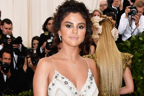 A woman with dark hair in an elegant dress poses at an event, surrounded by photographers.