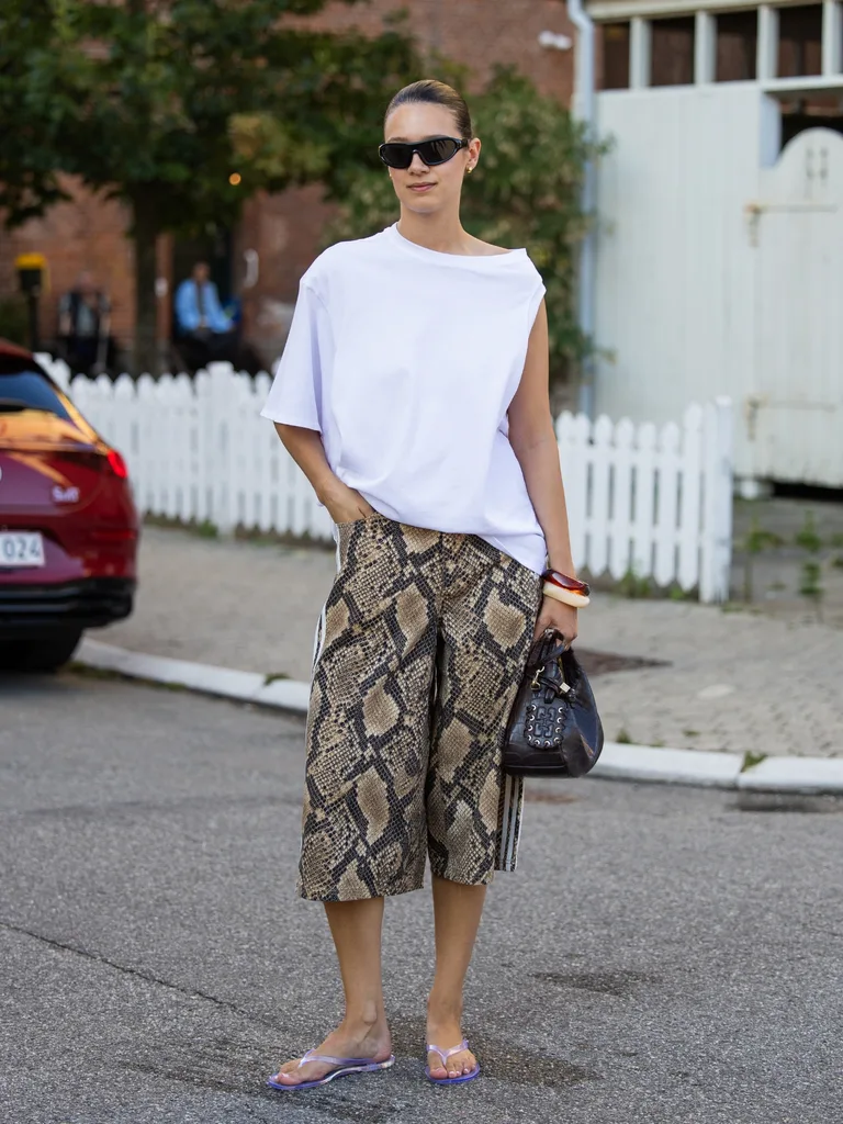 Woman wears oversized white t-shirt with 3/4 length snakeskin shorts and clear rubber thongs at Copenhagen Fashion Week