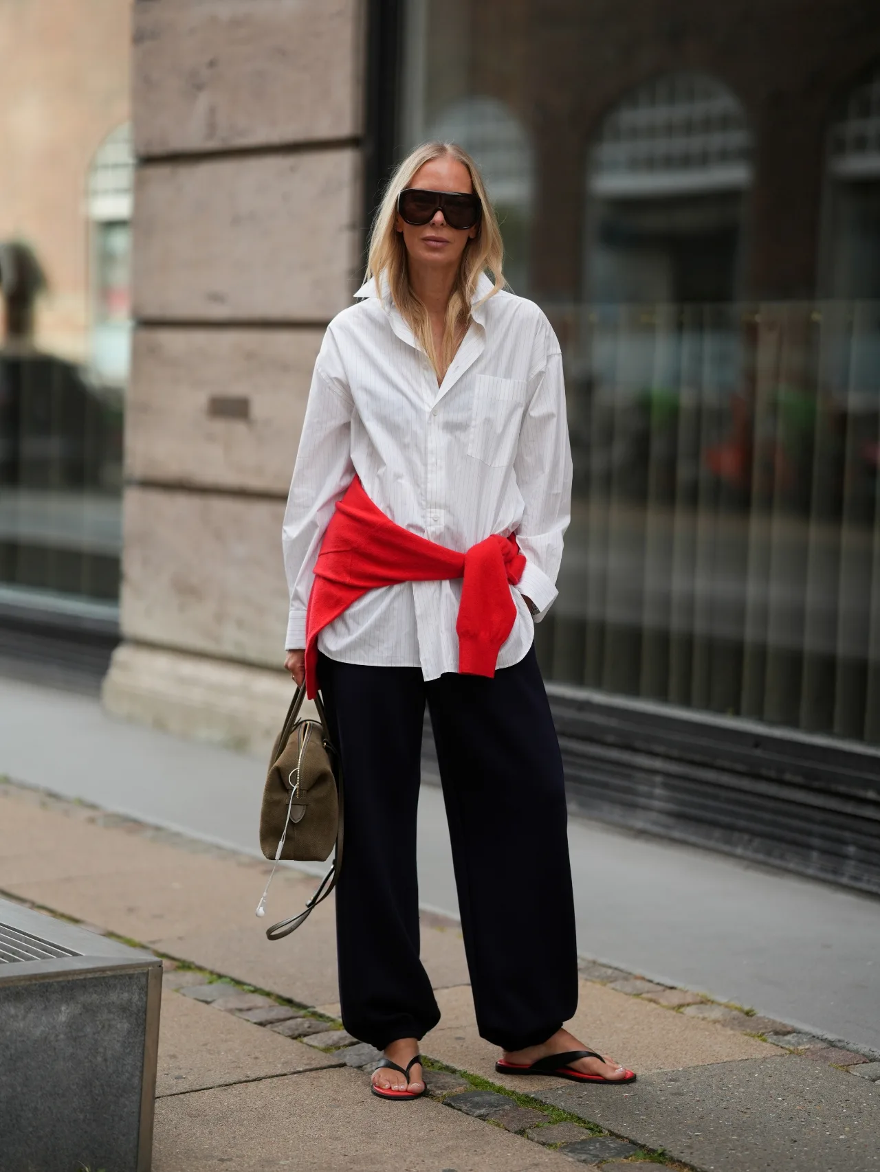 Woman wearing black thongs, white shirt, black trousers with red jumper tied around her waist