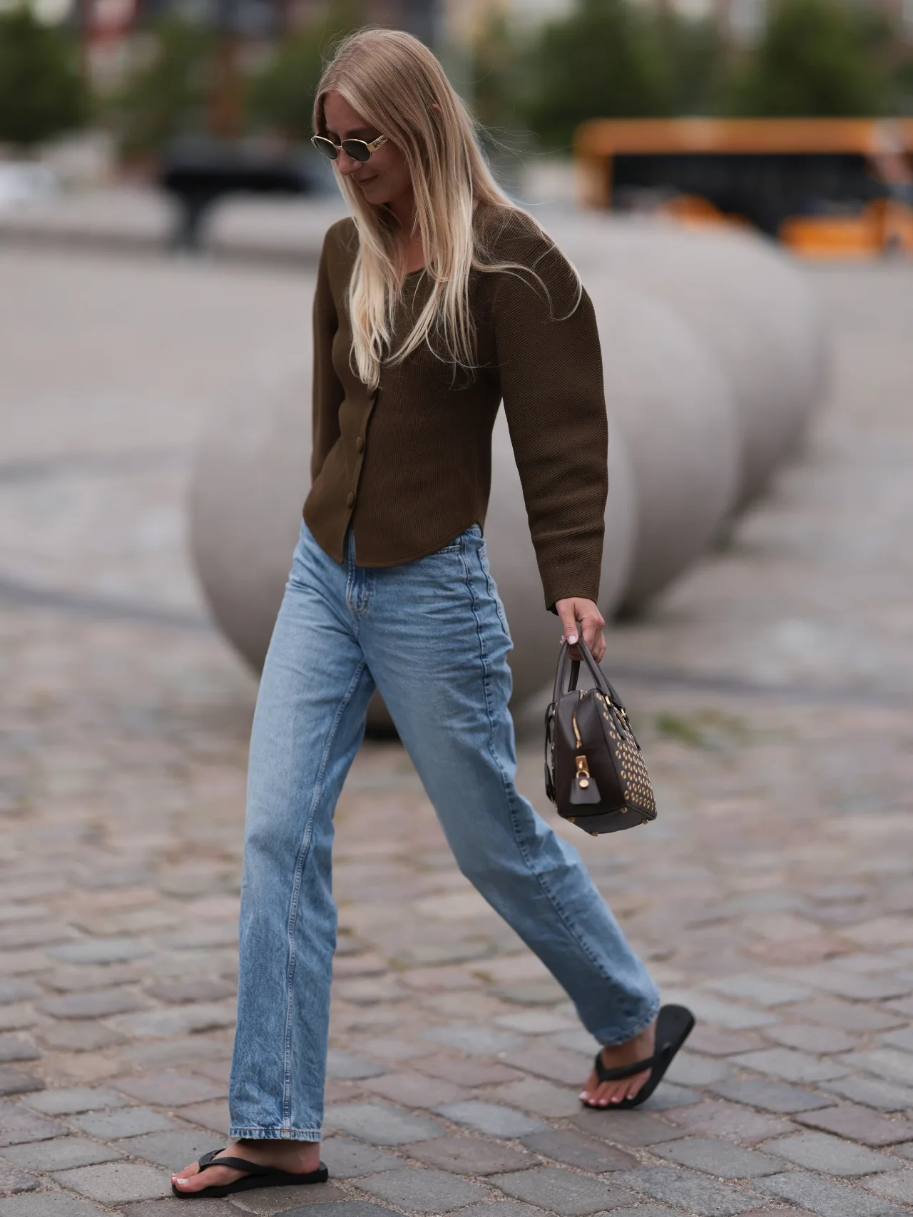 Woman wears straight-leg denim jeans, a brown fitted blazer and black flip flops at Fashion Week 