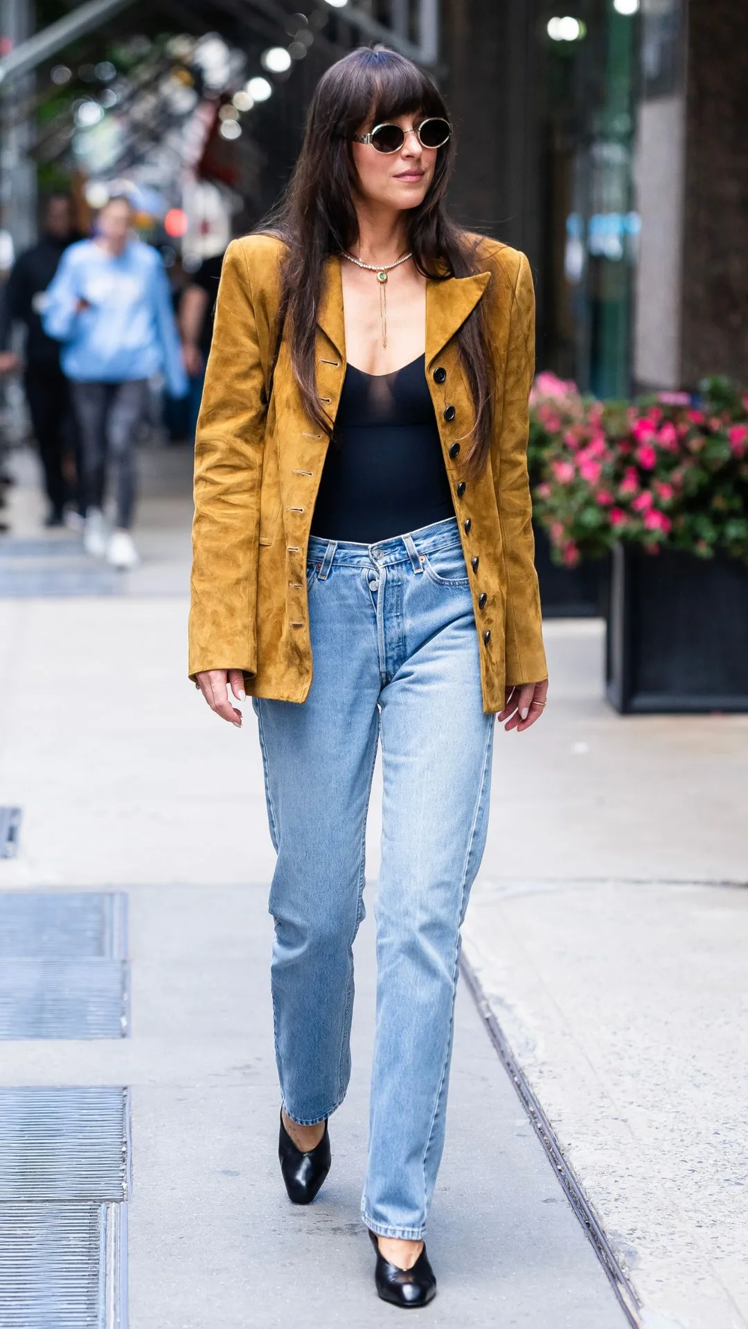 Woman wearing blue jeans and a mustard suede blazer walking