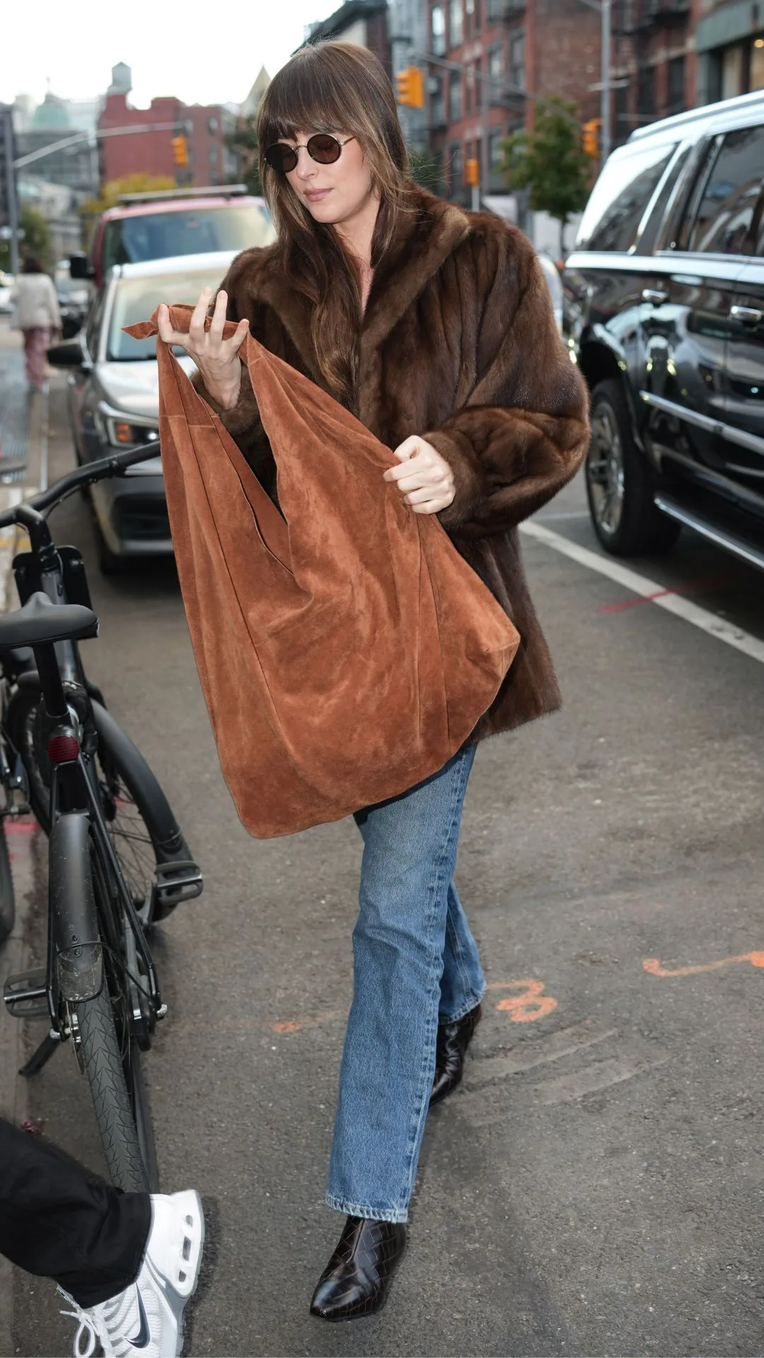 Woman walking on street wearing brown fur coat and blue jeans.