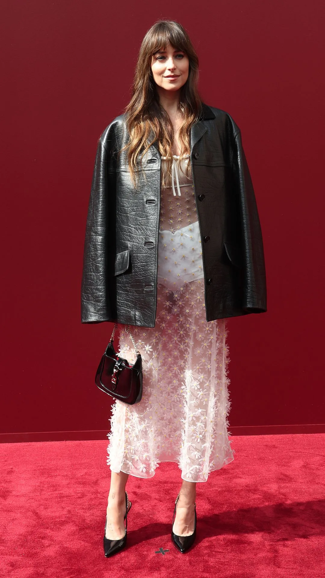 Woman wearing black leather jacket over sheer white dress.