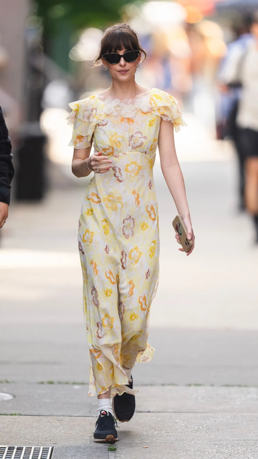 Woman walking on the street wearing sunglasses and yellow floral dress.