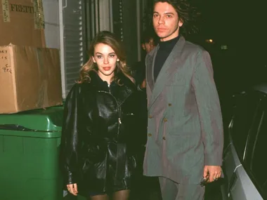 Kylie minogue wearing a leather jacket and leather mini skirt with Michael Hutchence, who's wearing a grey suit and black shirt, outside a Chanel fashion show in 1992.