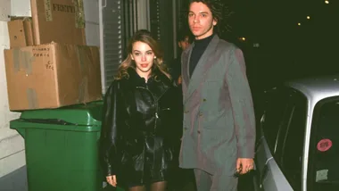 Kylie minogue wearing a leather jacket and leather mini skirt with Michael Hutchence, who's wearing a grey suit and black shirt, outside a Chanel fashion show in 1992.