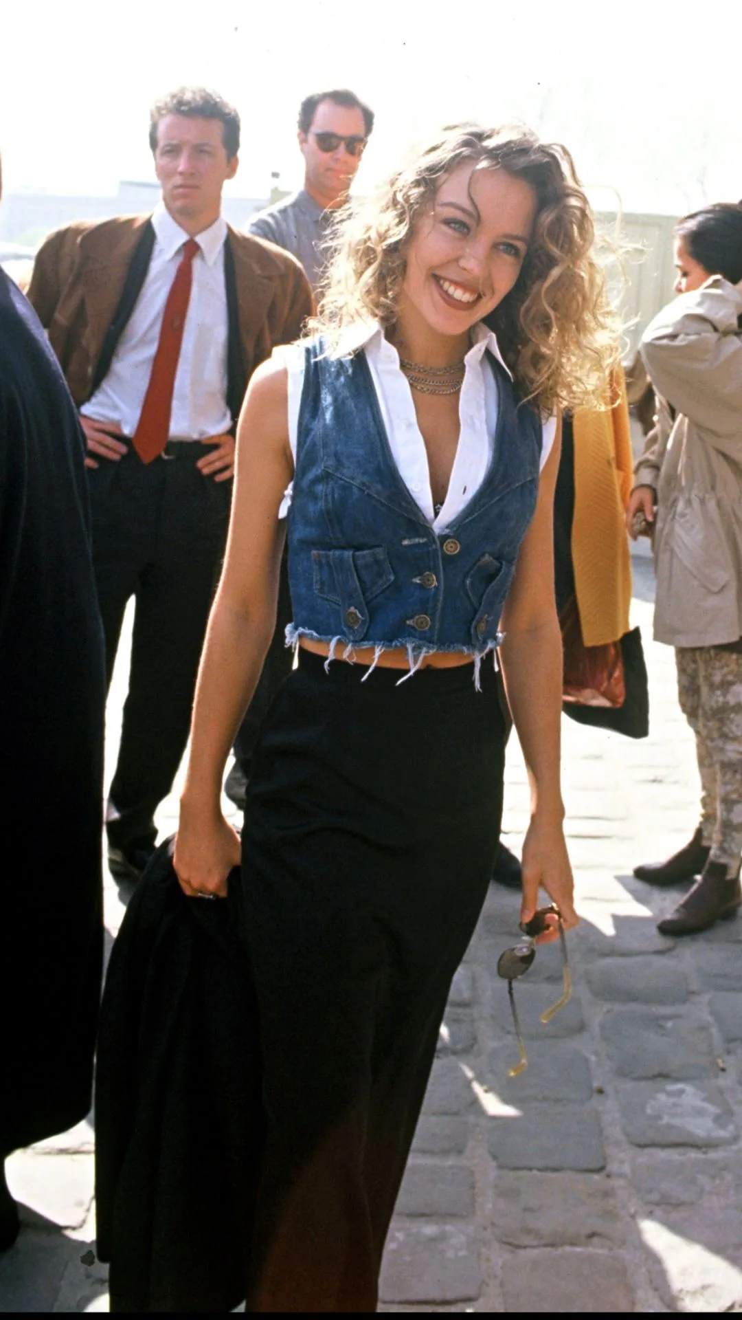 Kylie Minogue wearing a denim vest, white shirt and black skirt outside a fashion show in 1992.