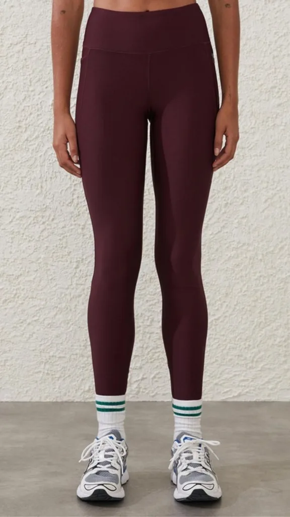 Cotton On Body Fleece Lined Full Length Tights have a mid-rsie waistband and are full length. This shade is a rich burgundy worn with white socks with emerald green stripes and white and grey sneakers for a trendy, sporty look. 