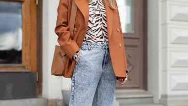 Acid wash jeans with a tan jacket and animal print blouse.