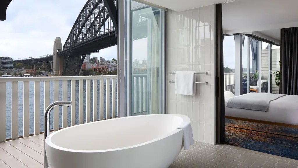 A view of the bathroom showing a freestanding bath with an open sliding door that looks out to the Sydney Harbour Bridge at the Pier One Hotel.