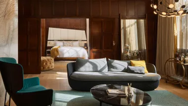 The Junior Suite at QT Sydney hotel. The image shows a living room with wooden paneling looking through to the bedroom in the distance.