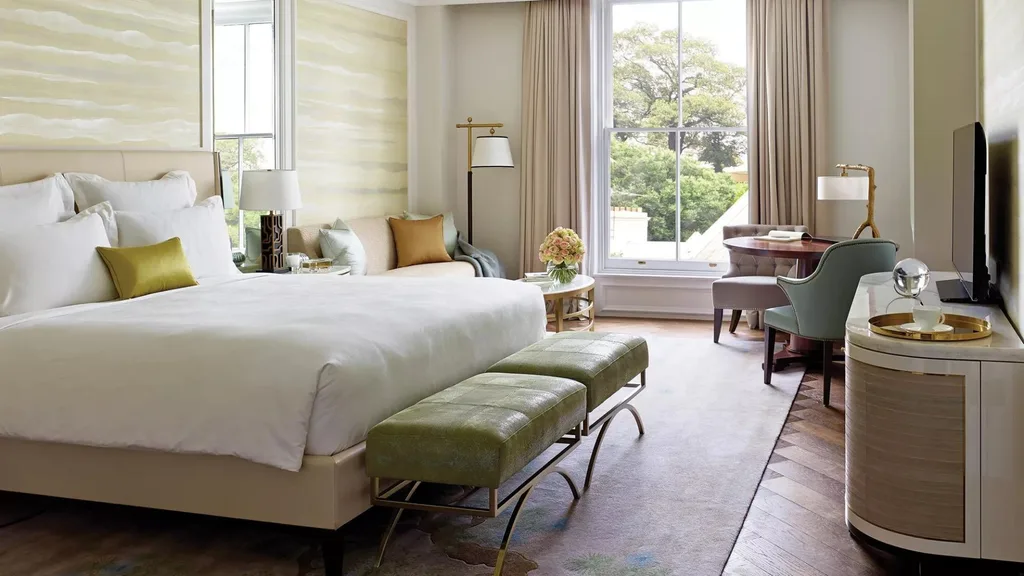 A suite at The Langham hotel in Sydney looking out to Sydney's Observatory Hill. The room is designed with modern regency-style decor including a large bed with cream patterned wallpaper