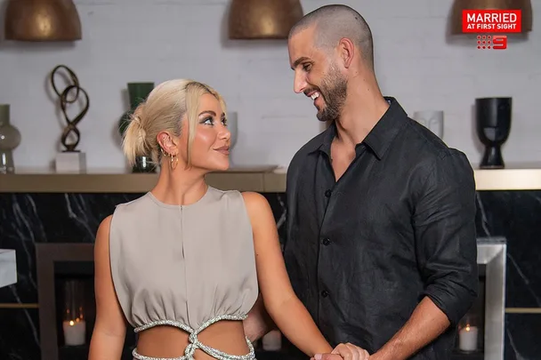 Couple smiling at each other with the "Married at First Sight" logo in the top right corner.